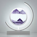 A modern circular LED light sculpture on a rectangular base, featuring a clear dome with purple watercolor mountain scenery inside, set against a minimalist gray background.