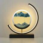 A modern LED arc lamp with a circular acrylic display showing a mountain landscape, mounted on a black rectangular base with a gold support rod.